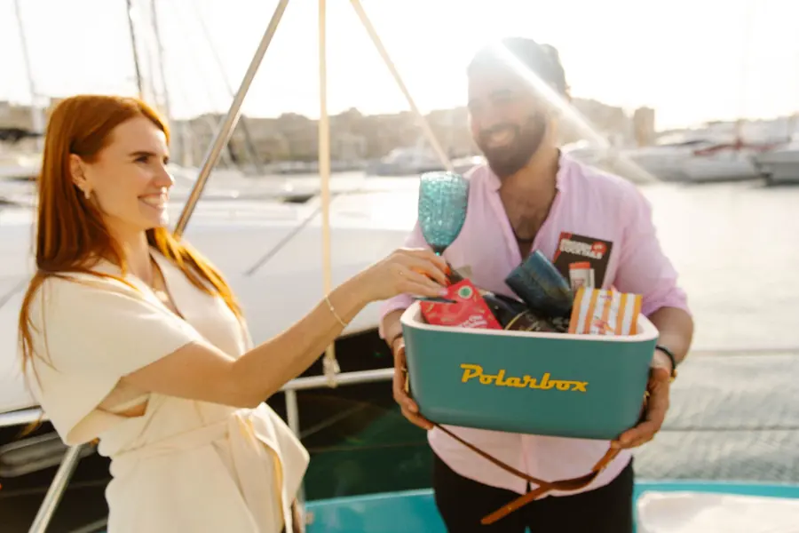 Host handing over a welcome cooler with drinks to a guest on deck